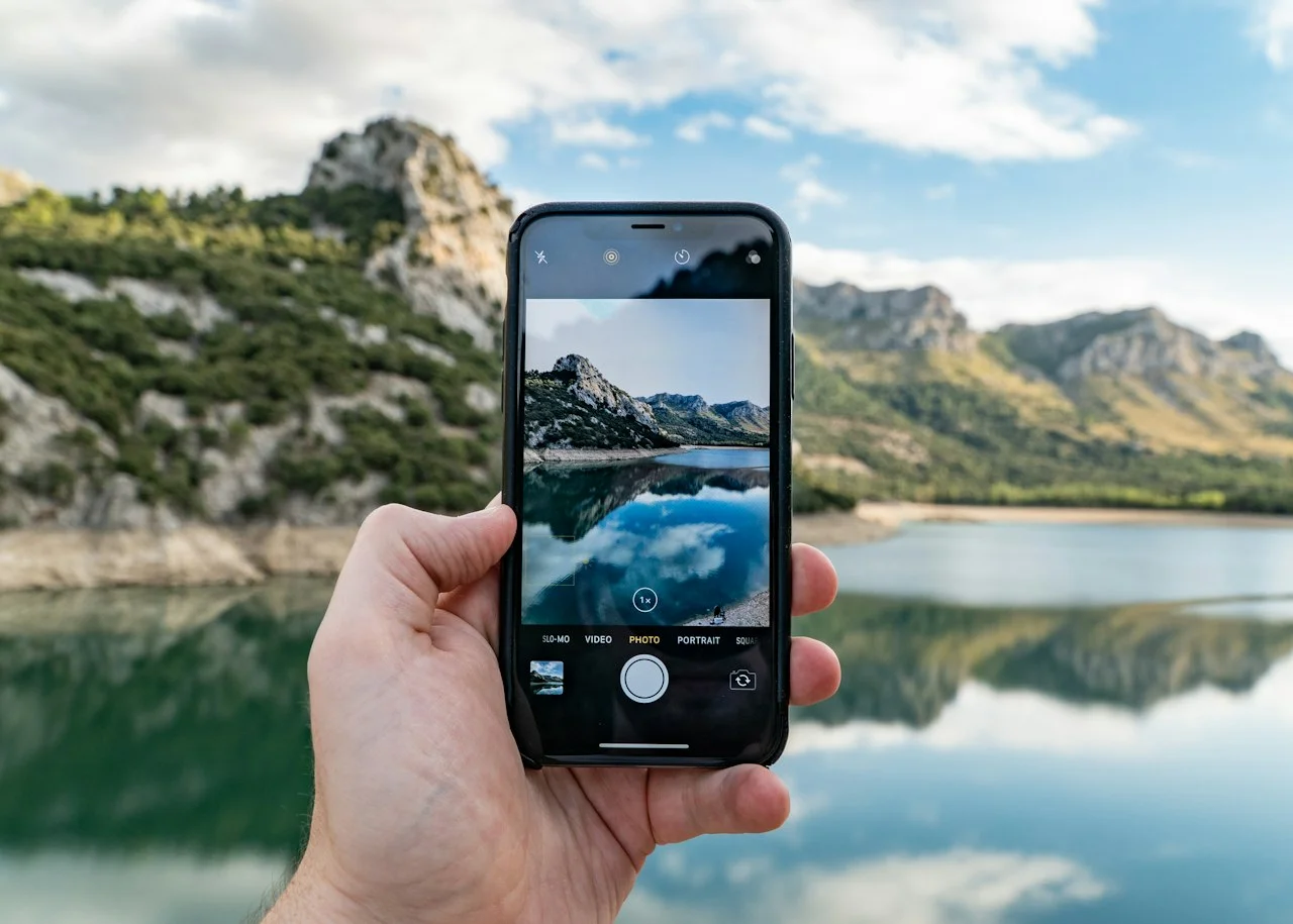 Dłoń trzyma telefon, na ekranie zdjęcie jeziora i gór