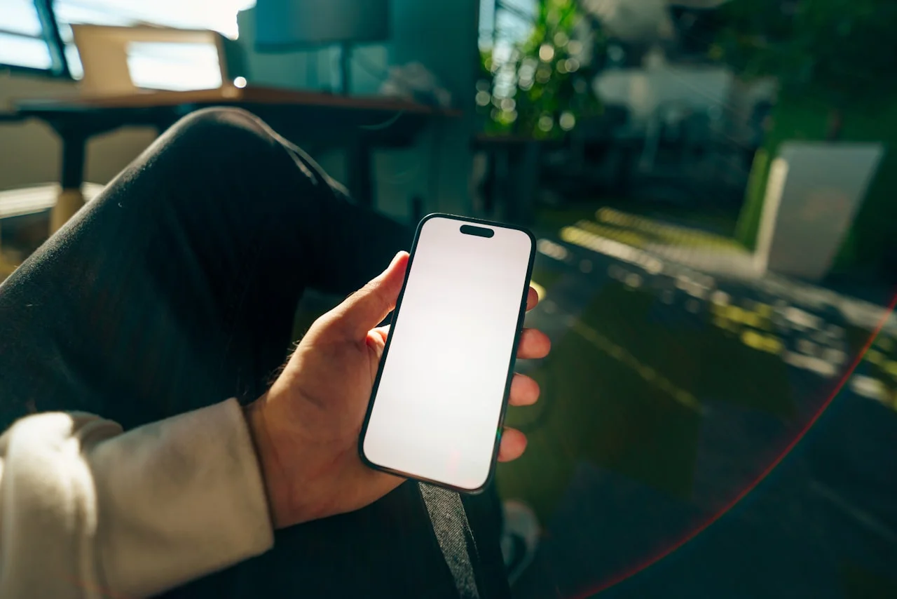 Dłoń trzyma telefon z bardzo jasnym ekranem przy świetle dziennym