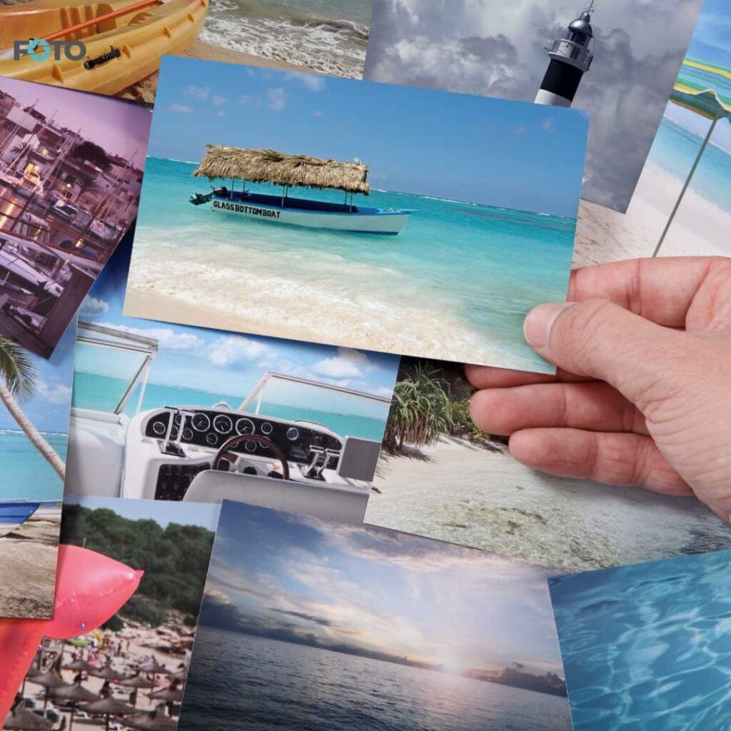 Roka drži natisnjeno fotografijo tropske plaže z ladjo med drugimi potovalnimi fotografijami